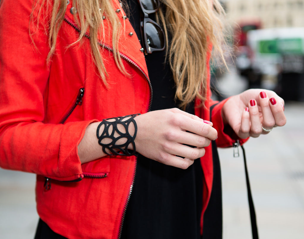 Woman wearing a recycled rubber bracelet from Paguro Upcycle with a red jacket and black dress