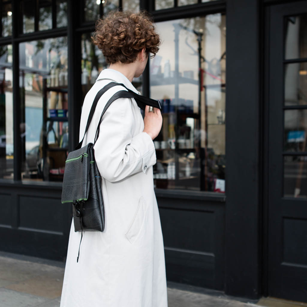 Stylish woman wearing a Paguro Upcycle recycled rubber crossbody bag on a city street, showcasing eco-friendly fashion