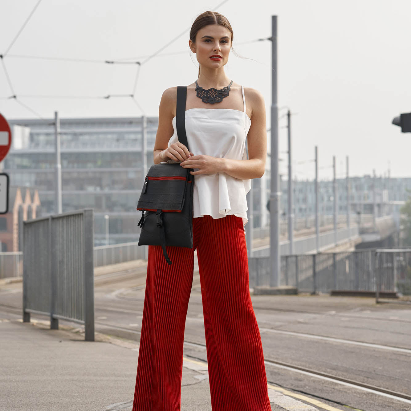 Stylish model wearing a Paguro Upcycle recycled rubber crossbody bag with a chic outfit and bold red trousers
