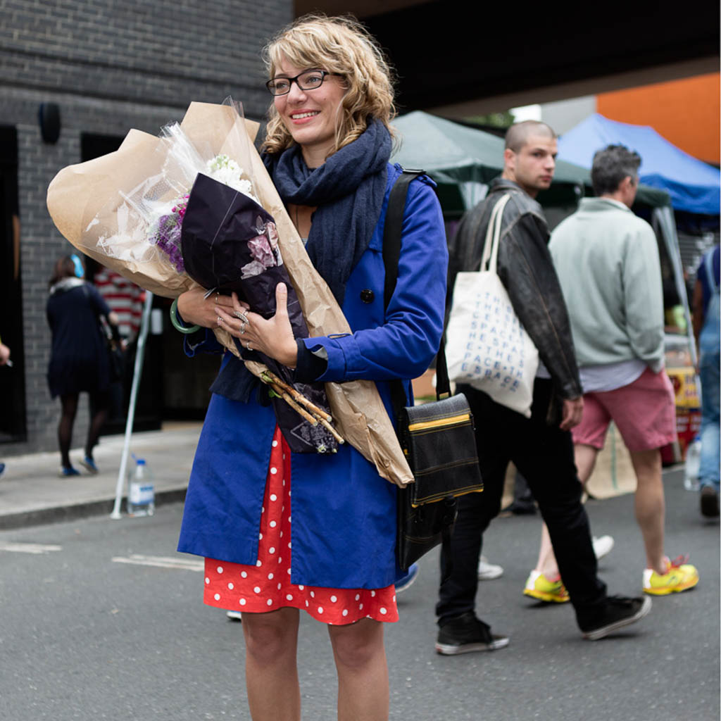 Stylish woman holding flowers with a Paguro Upcycle recycled rubber crossbody bag at an outdoor market