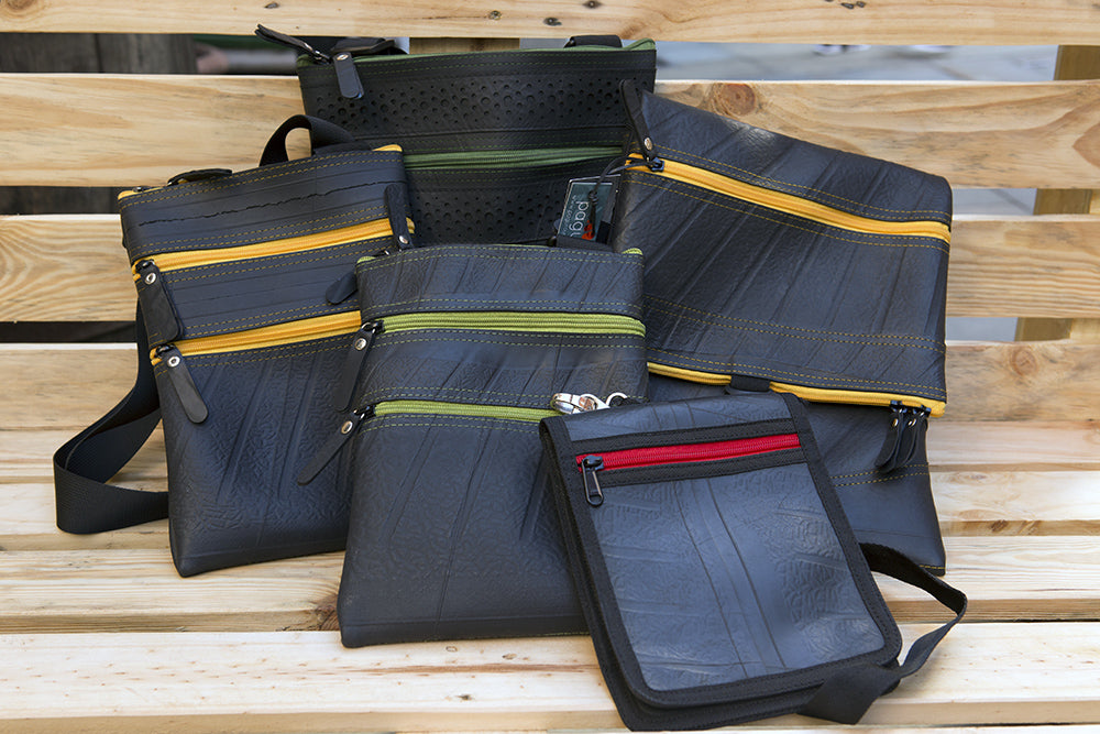 Paguro Upcycle upcycled vegan crossbody bag collection with multiple colors and zippers displayed on wooden bench