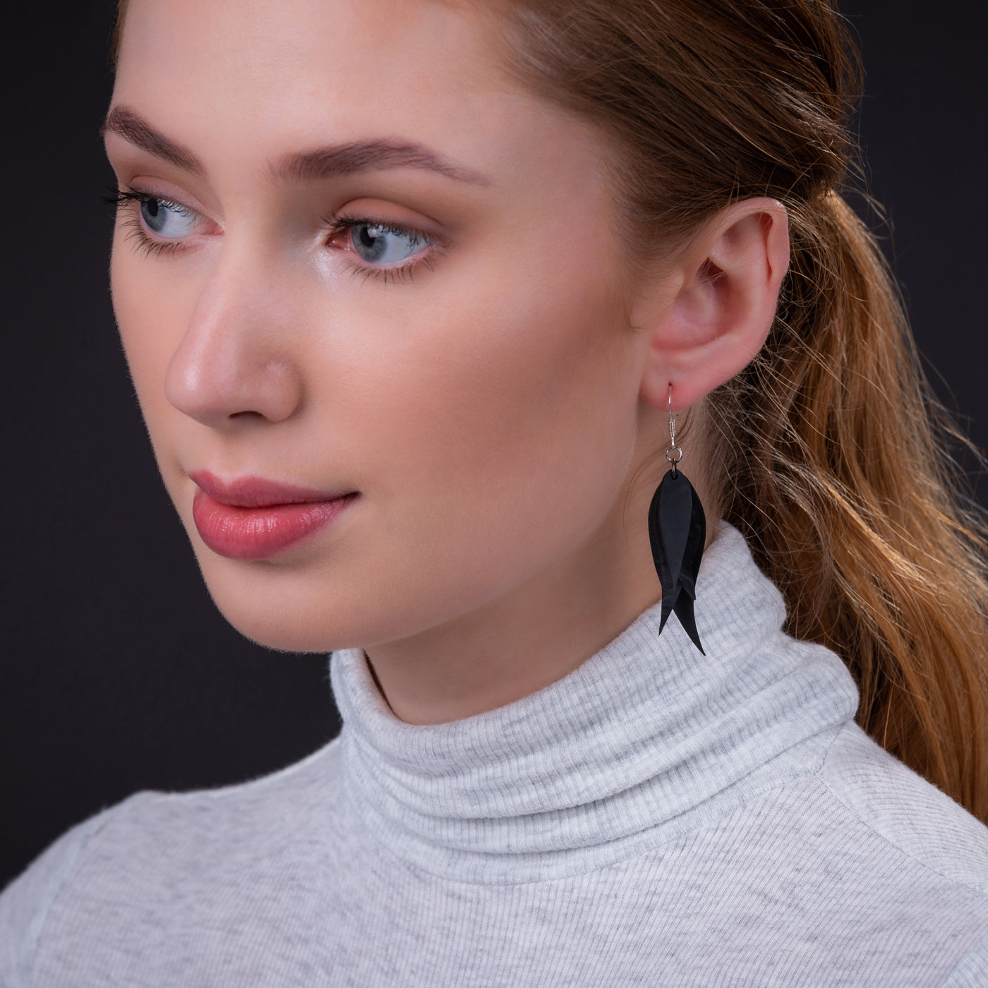 Woman wearing recycled rubber earrings from Paguro Upcycle with black leaf-shaped design