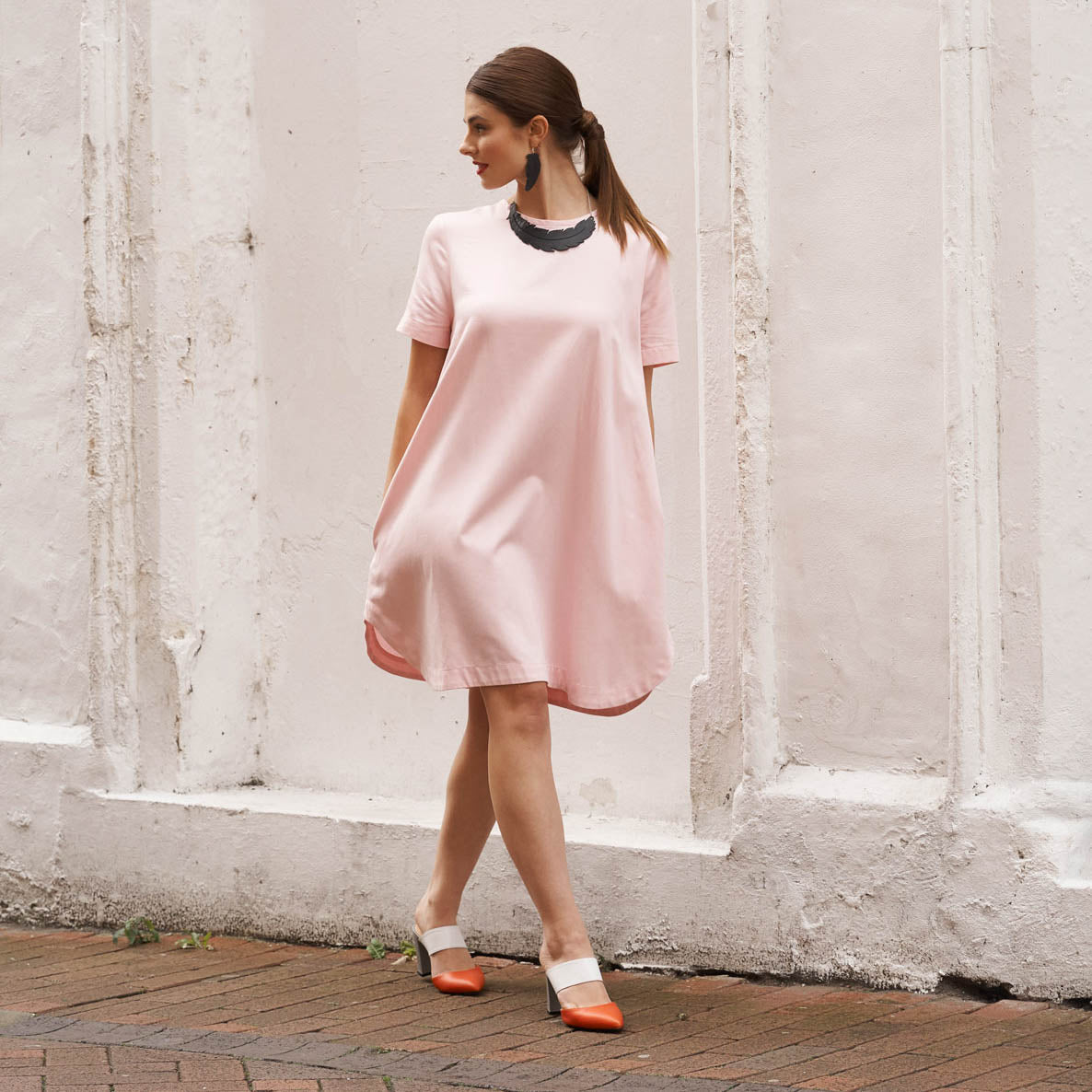 Woman wearing upcycled rubber feather earrings from Paguro Upcycle with a pink dress and two-tone shoes