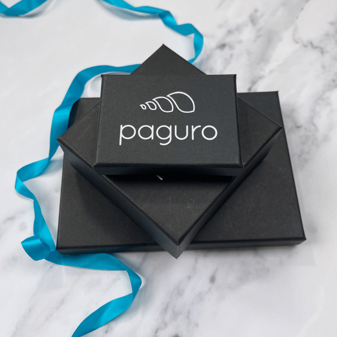 Black Paguro Upcycle earring boxes stacked on marble surface with blue ribbon showcasing sustainable packaging