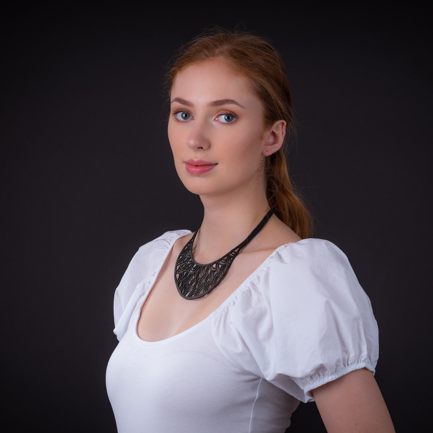 Model wearing Paguro Upcycle black upcycled inner tube necklace crescent statement piece with white puff sleeve top
